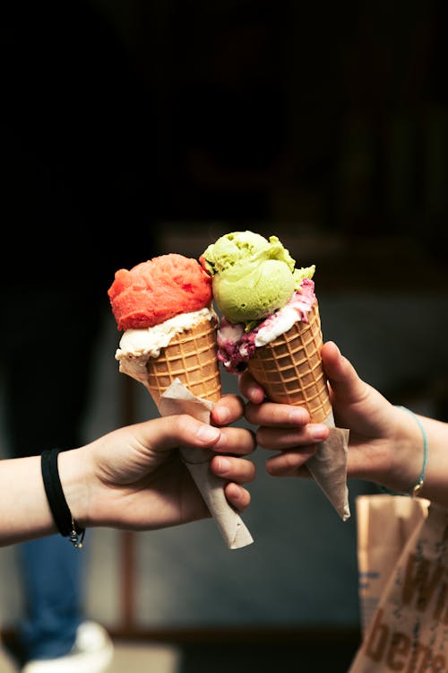 Two hands holding ice cream cones with colorful toppings