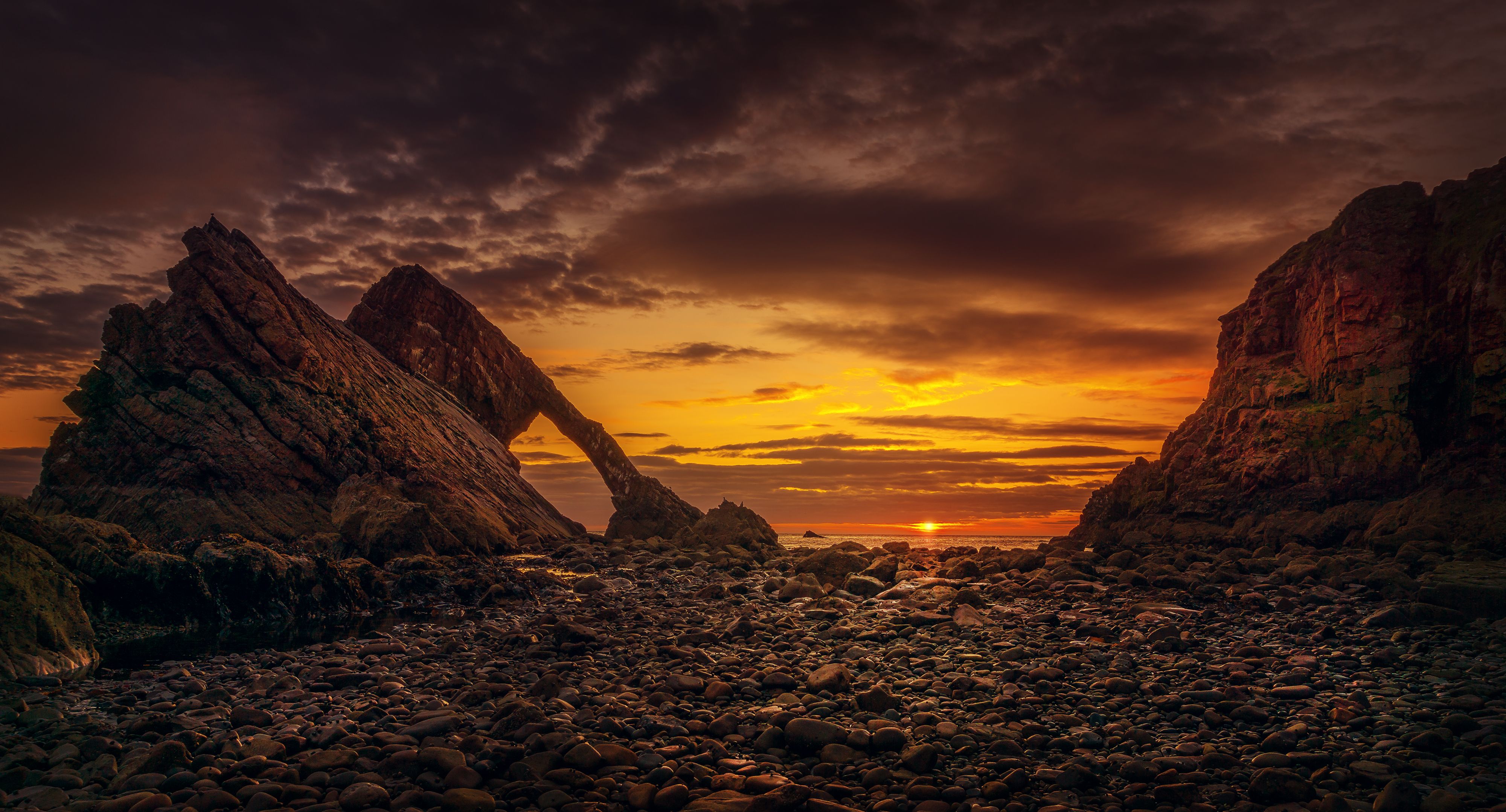 Stunning sunset view of Bow Fiddle Rock, a dramatic sea arch formation on Scotland's rocky coast.