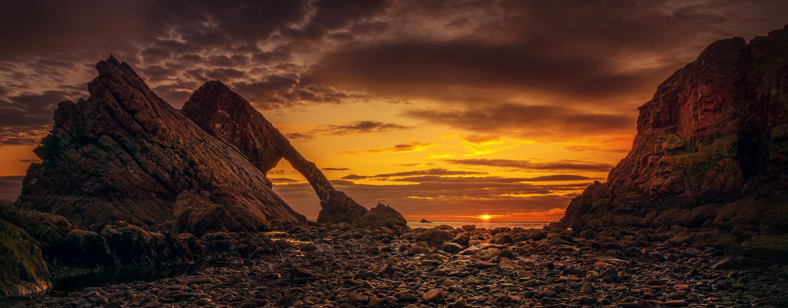 Stunning sunset view of Bow Fiddle Rock, a dramatic sea arch formation on Scotland's rocky coast.