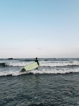 A lone surfer carrying a board ventures into the waves of a pristine Brazilian beach.