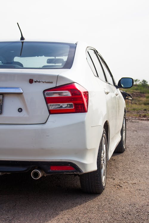 The rear end of a white car parked on a dirt road