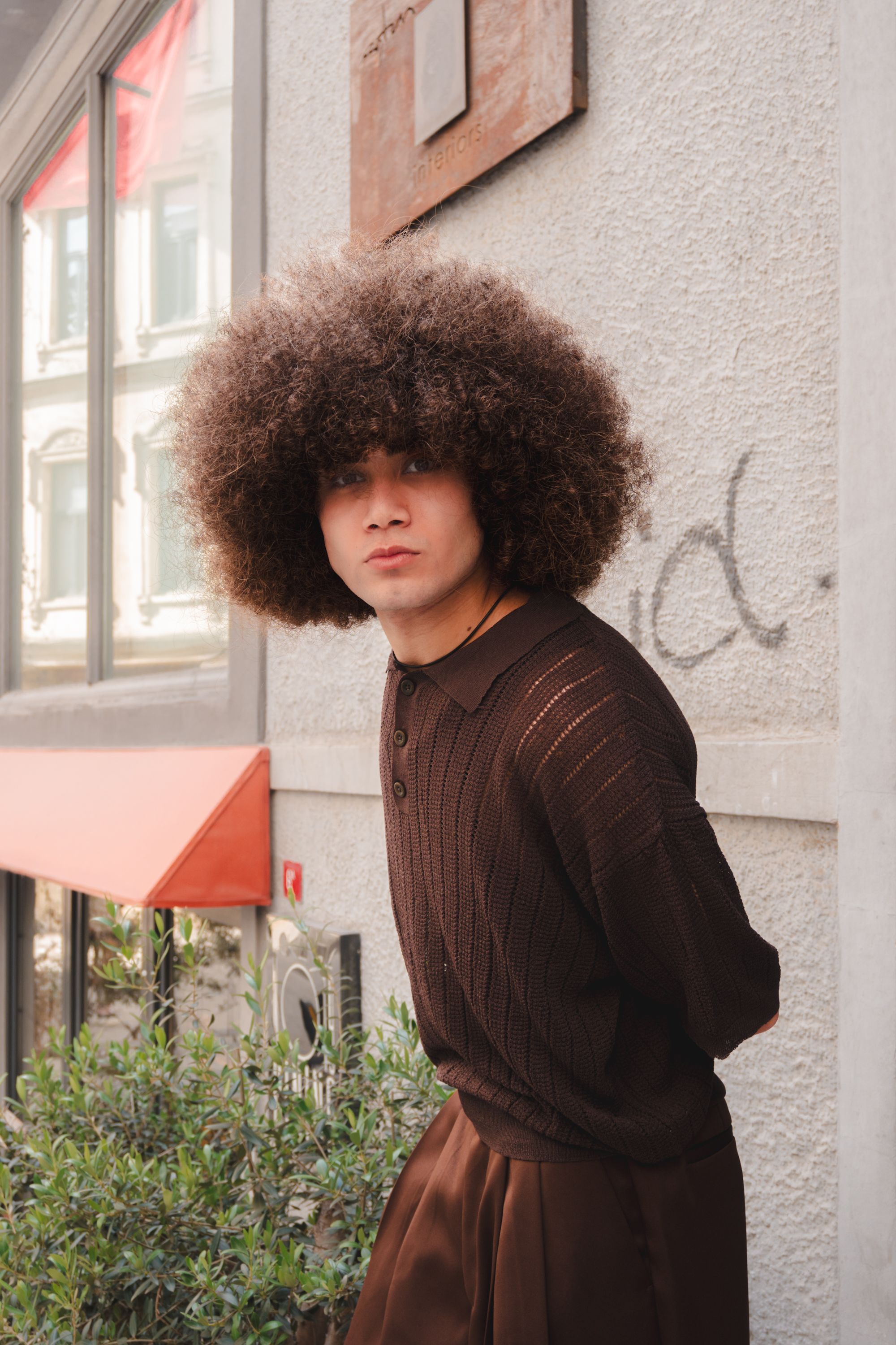 Portrait of a stylish young man with curly hair in an urban environment, showcasing individuality and fashion sense.