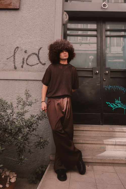 Free Stylish young man with an afro in brown attire posing confidently by a building entrance. Stock Photo