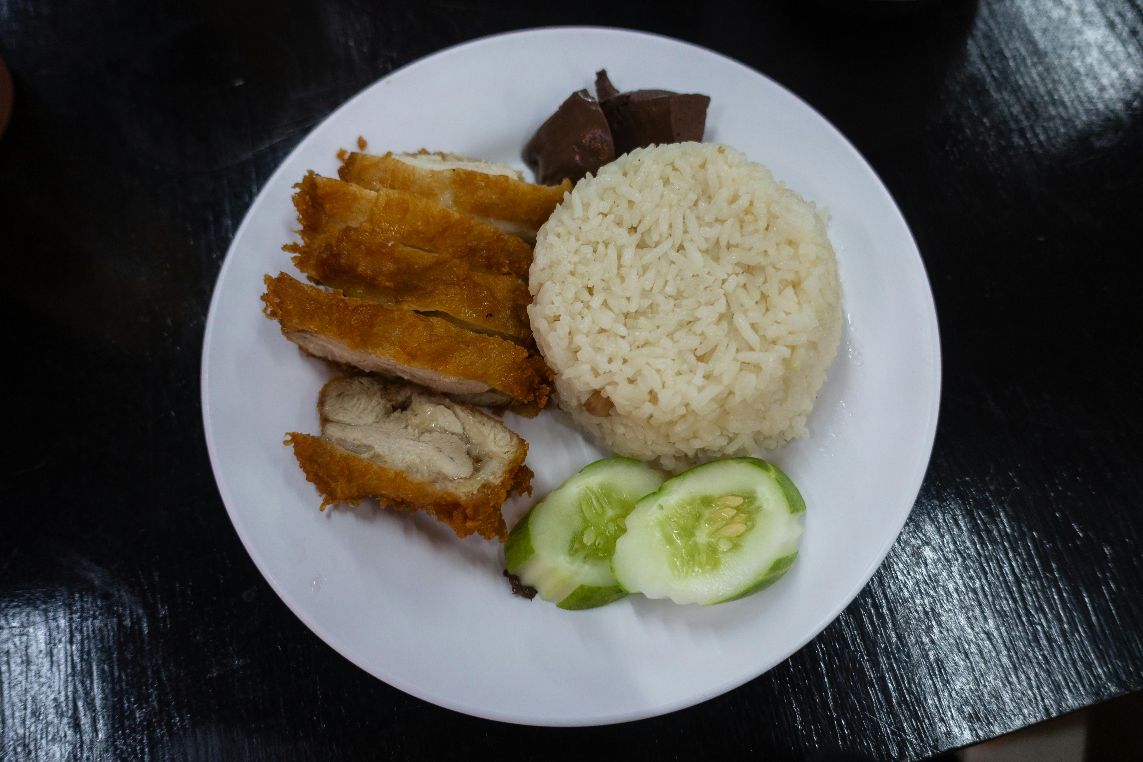 Roasted chicken rice plate with chilli sauce, ginger paste and cucumber served at a Singapore hawker centre