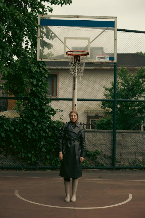 Young Woman Wearing a Black Overcoat Standing under a Basketball Hoop