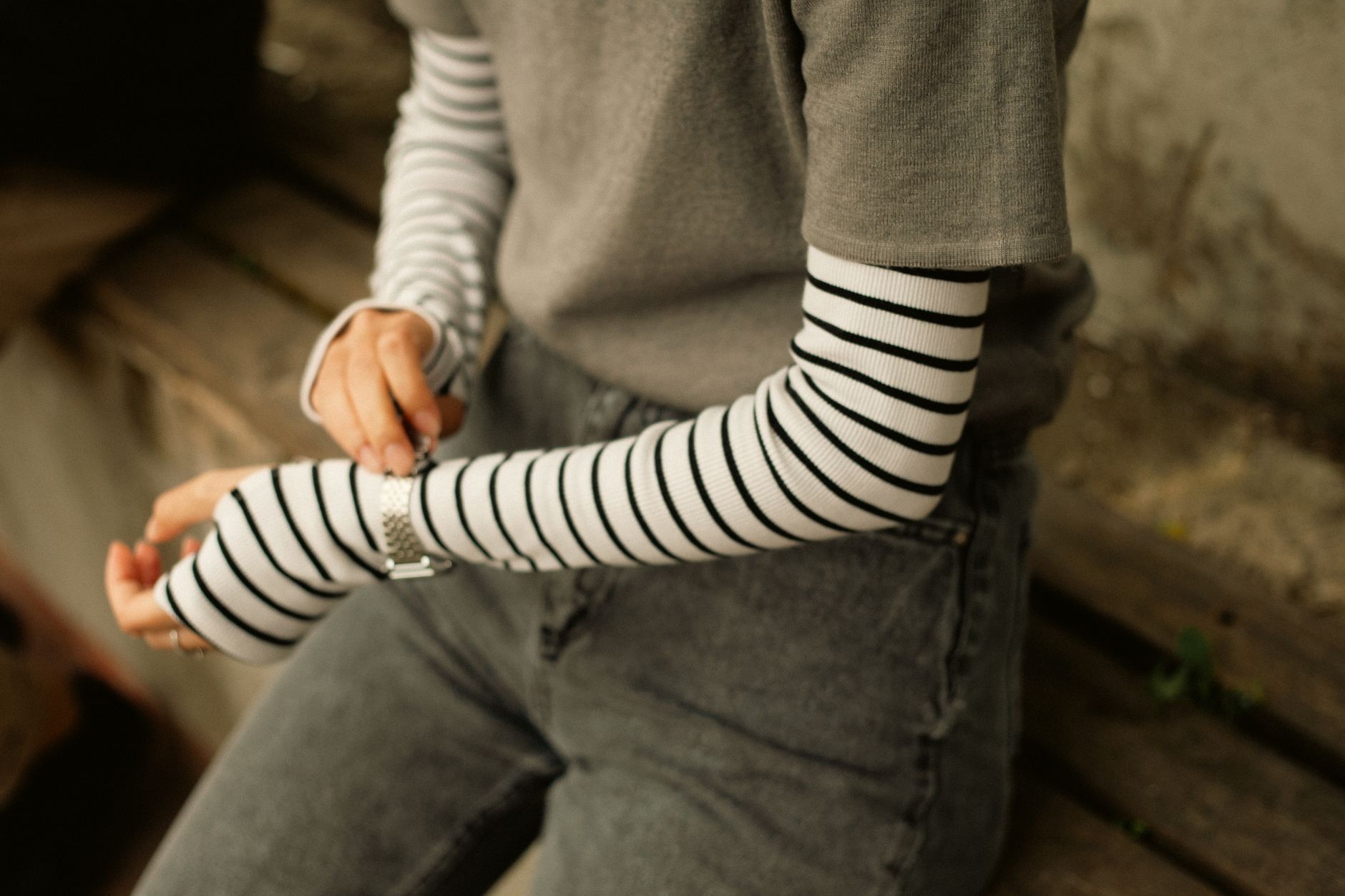 Young woman adjusting wristwatch with striped sleeves in outdoor setting.
