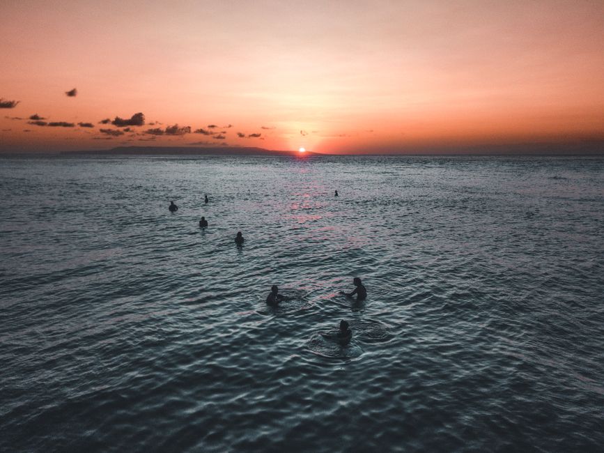 Peaceful evening scene with silhouettes swimming in the ocean during sunset, showcasing vibrant colors and tranquil atmosphere.