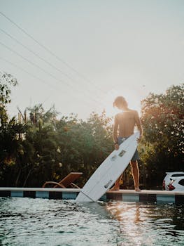 一名年轻人拿着冲浪板，站在阳光照射的户外泳池边