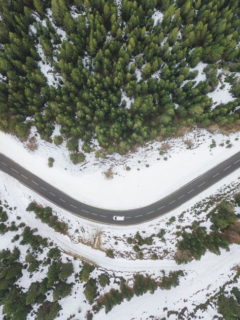 An aerial shot of a winding road through a snowy forest offers a serene winter landscape.