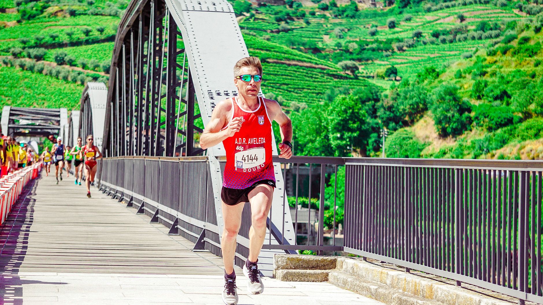 A focused athlete running across a scenic bridge during a marathon in a lush outdoor setting.