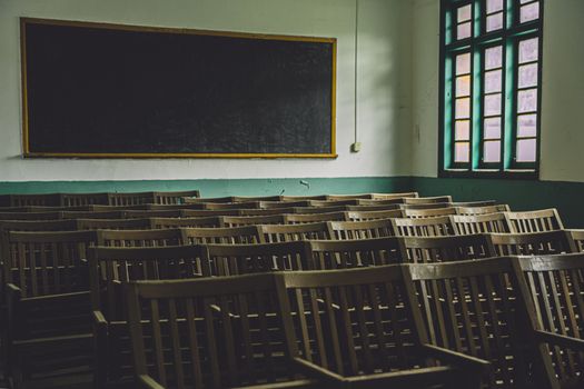 Empty vintage classroom with wooden chairs, large blackboard, and windows.