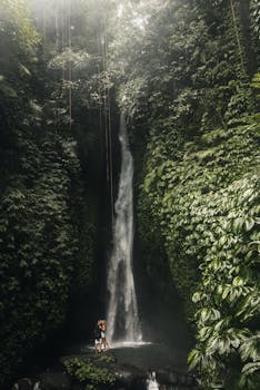 一对夫妇在郁郁葱葱的热带瀑布底部拥抱，周围环绕着茂密的绿色植物