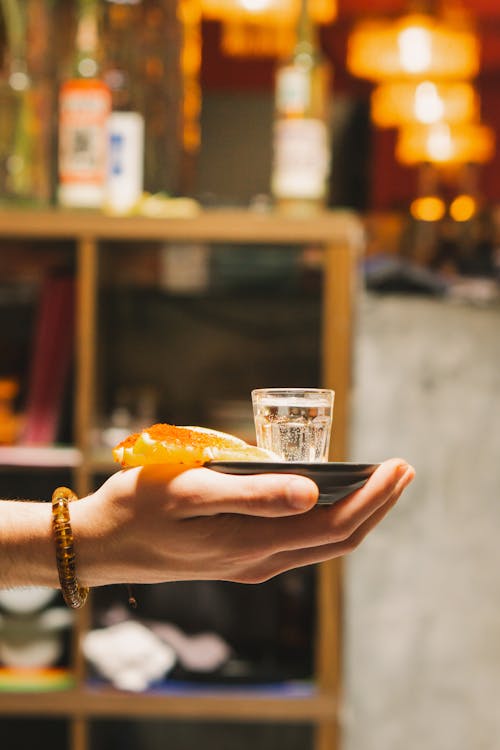 A person holding a small plate with a shot glass