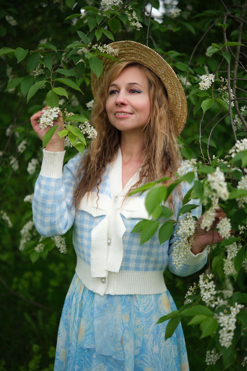 Portrait of a woman in a garden wearing a straw hat and blue dress.