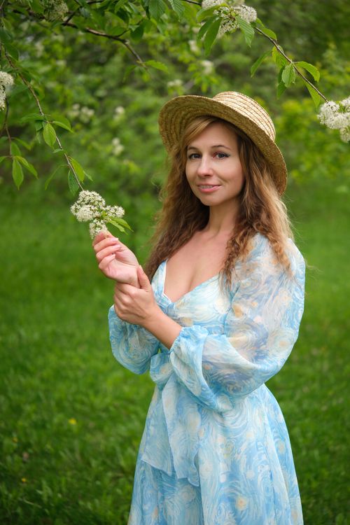 Free Portrait of a woman in a blue sundress and straw hat holding flowers outdoors. Stock Photo