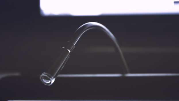 Minimalist close-up of a metallic gooseneck light fixture in dark ambiance.