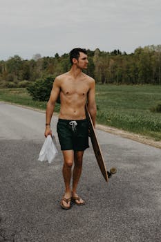 年轻的运动员扛着滑板，在乡村道路上享受户外休闲娱乐