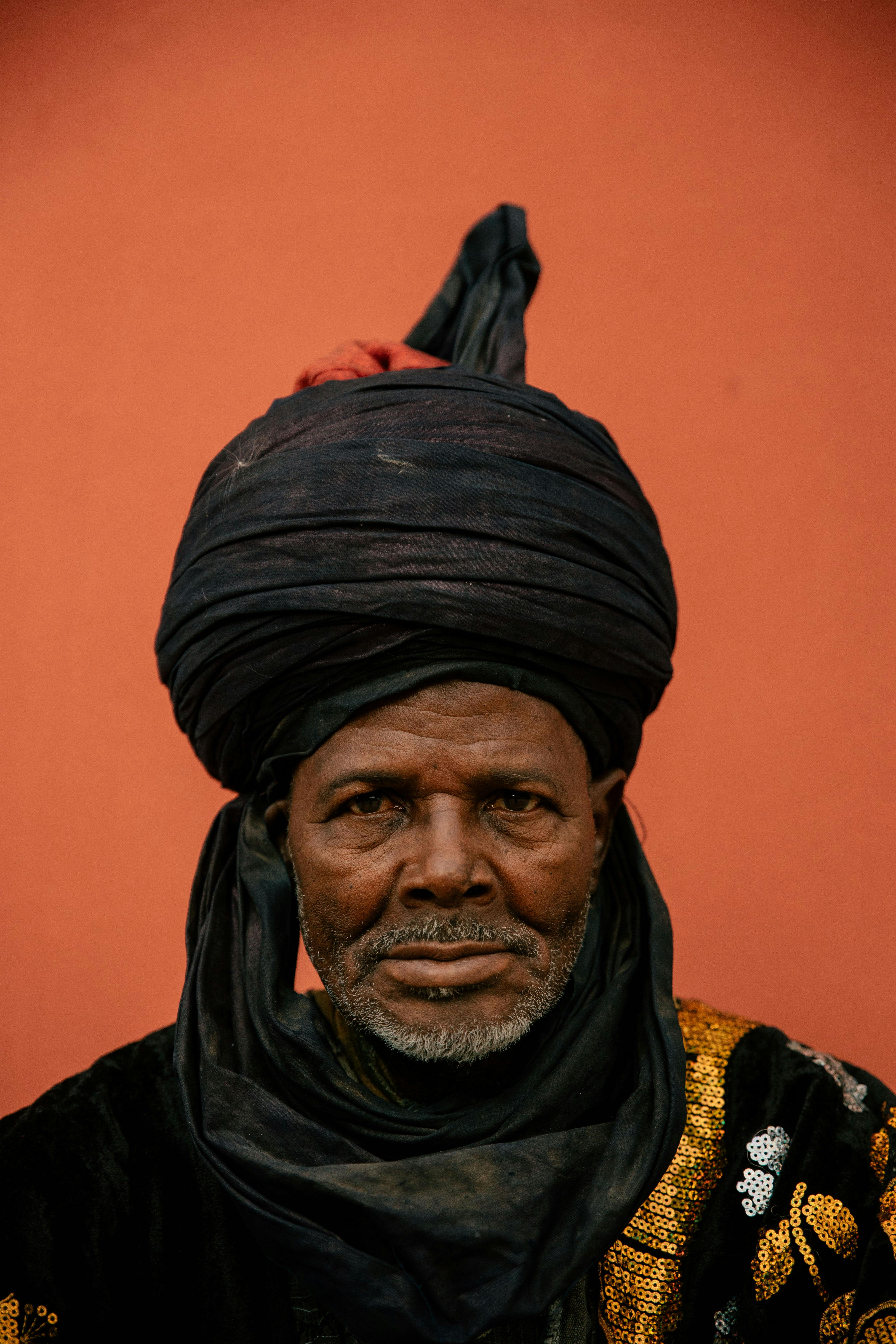 Studio portrait of an adult man wearing a traditional turban against an orange background.