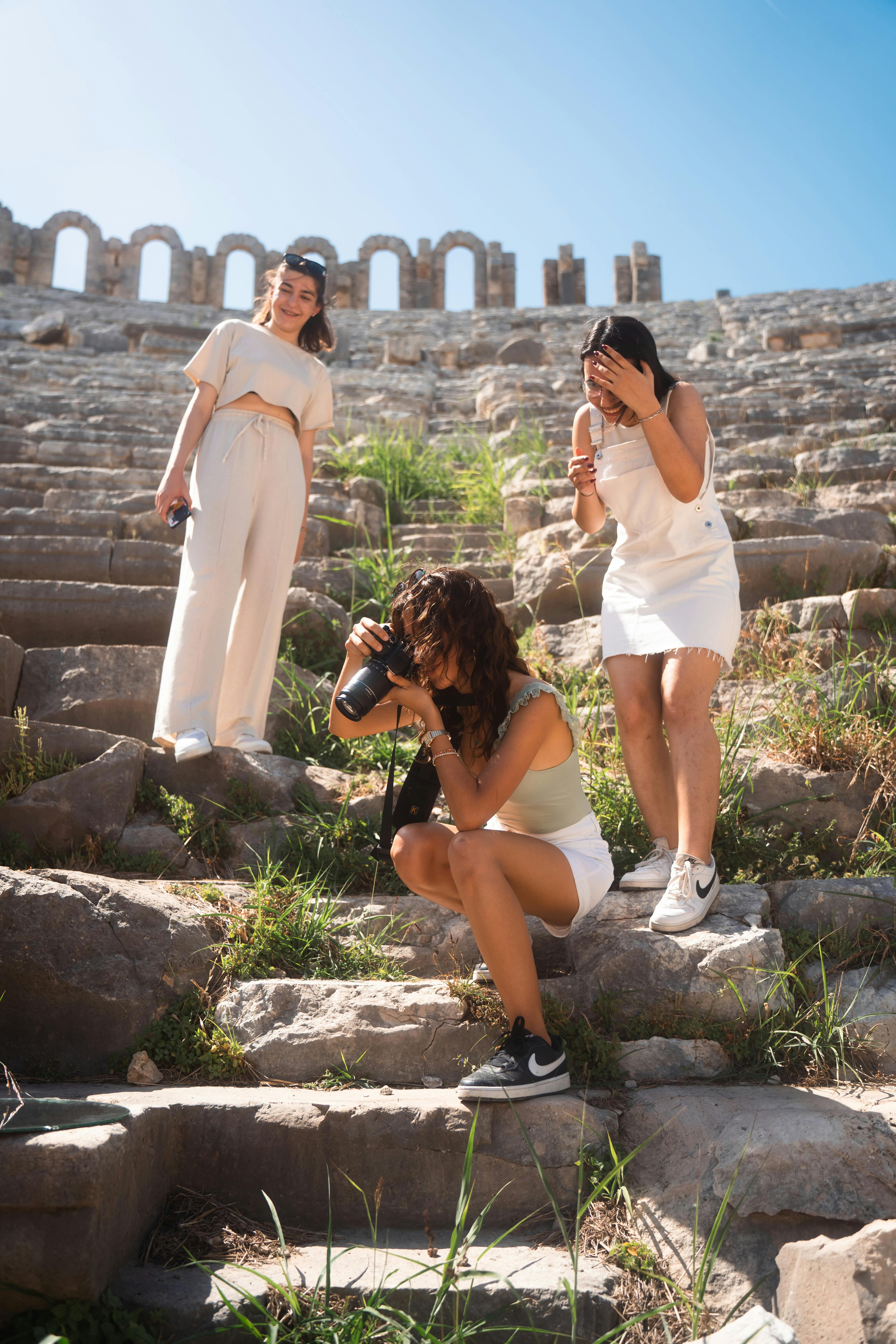 Free Three young women enjoying photography at an ancient amphitheater on a sunny day. Stock Photo