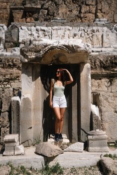 Young woman poses at an ancient archaeological site with ruins, bathed in summer sunlight.