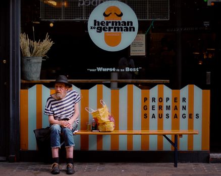 Man seated outside 'Herman ze German' shop in London, enjoying urban street view.