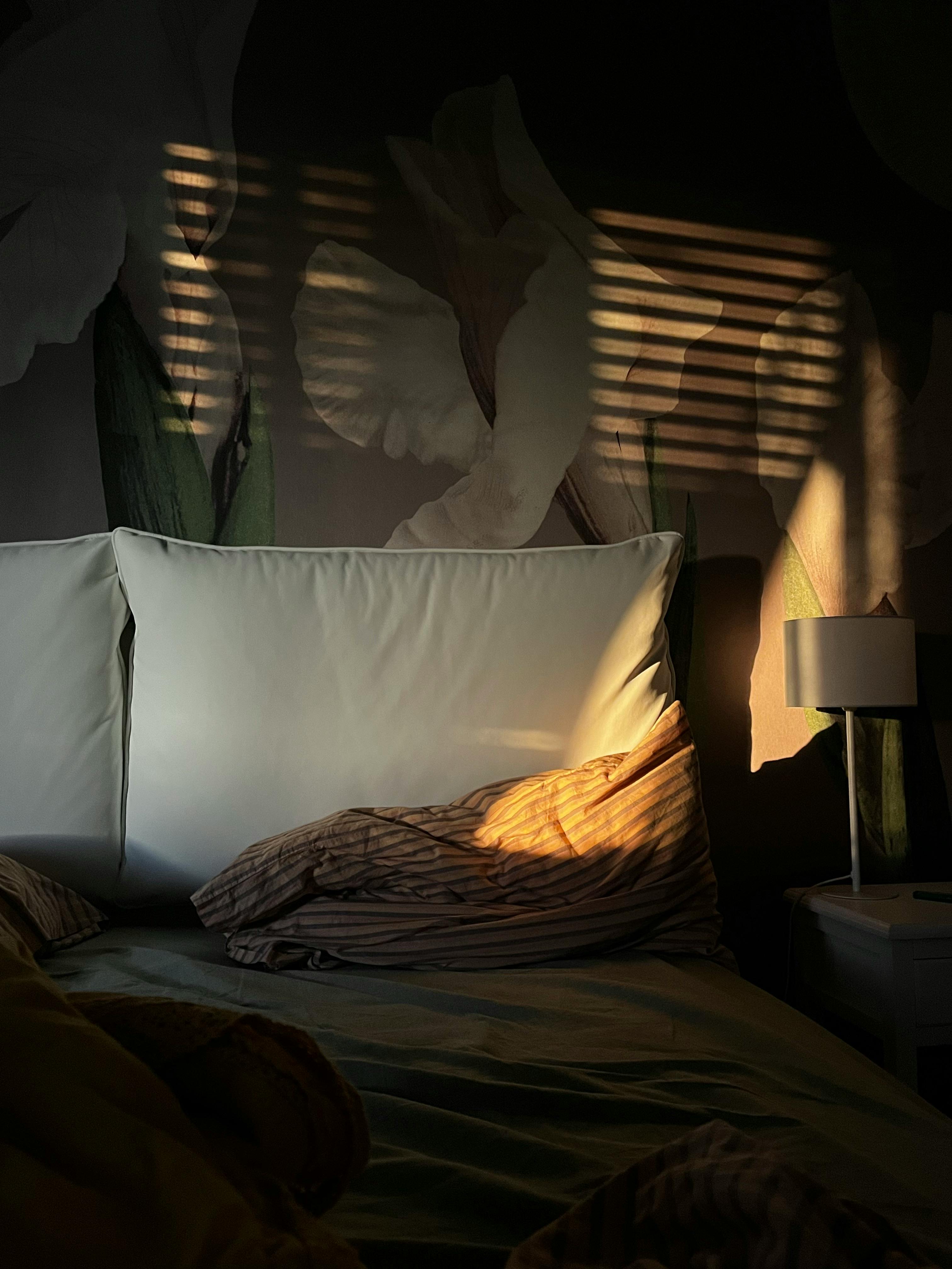 A serene bedroom scene with sunlit pillows and soft shadows creating a tranquil atmosphere.