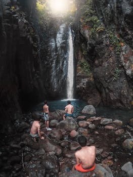 Four young men explore a serene waterfall in Como, Lombardy. An enchanting nature scene.