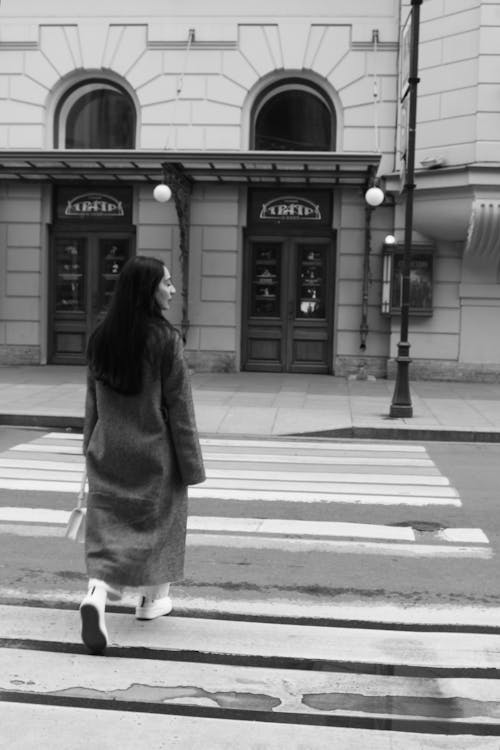 A woman walking across the street in a long coat