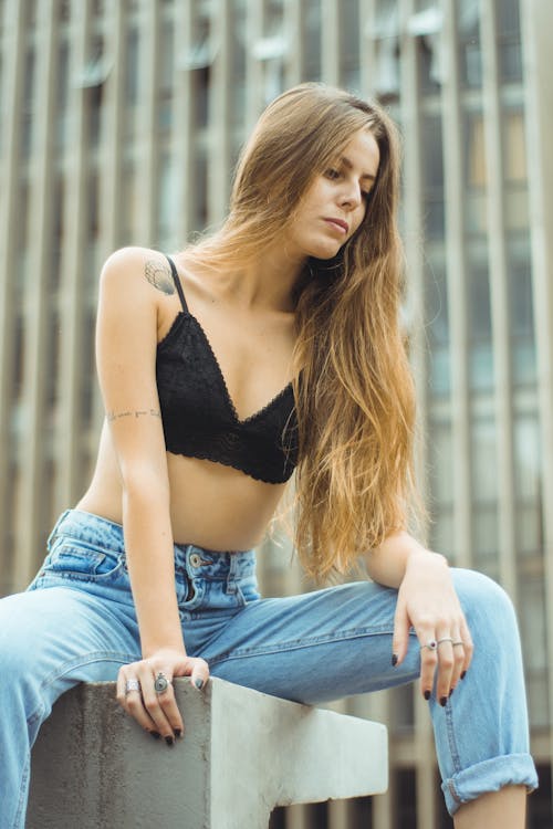 Free Woman Sitting on Concrete While Wearing Denim Jeans and Black Bralette Stock Photo