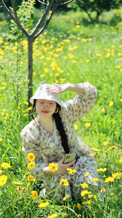 A woman in a hat and dress sitting in a field of flowers