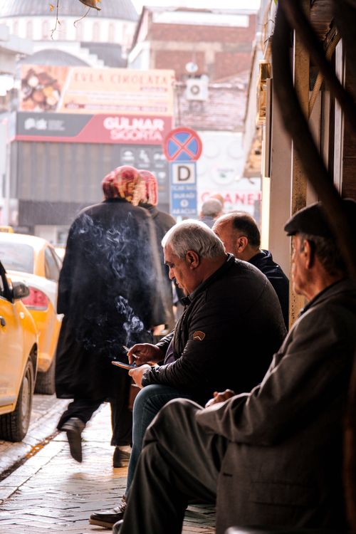 Free Elderly men sitting on a sidewalk, socializing in a busy urban environment with city hustle and bustle. Stock Photo