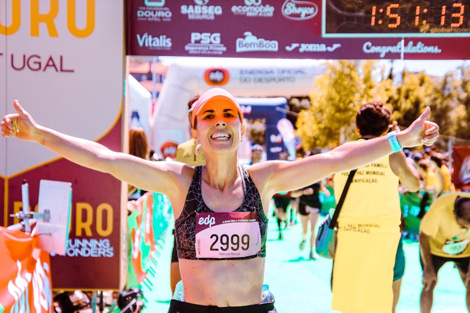 A joyous woman celebrates crossing the marathon finish line with arms raised in victory.