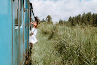 一位身着休闲服的女人从火车车窗探出身来，四周绿意盎然，捕捉到了旅行与冒险的精神