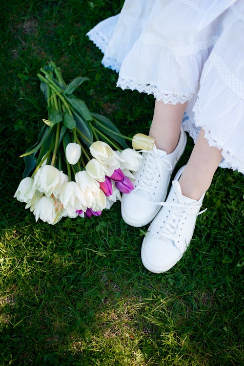 Feet of a Girl Wearing White Shoes Sitting by a Bunch of Freshly Picked Tulips