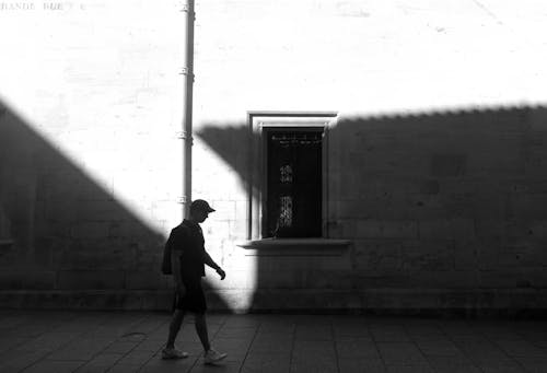 A man walking down the street in the shadow of a building