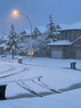 Winter scene of a snow-covered street in Calgary, Canada with houses and streetlights at twilight.