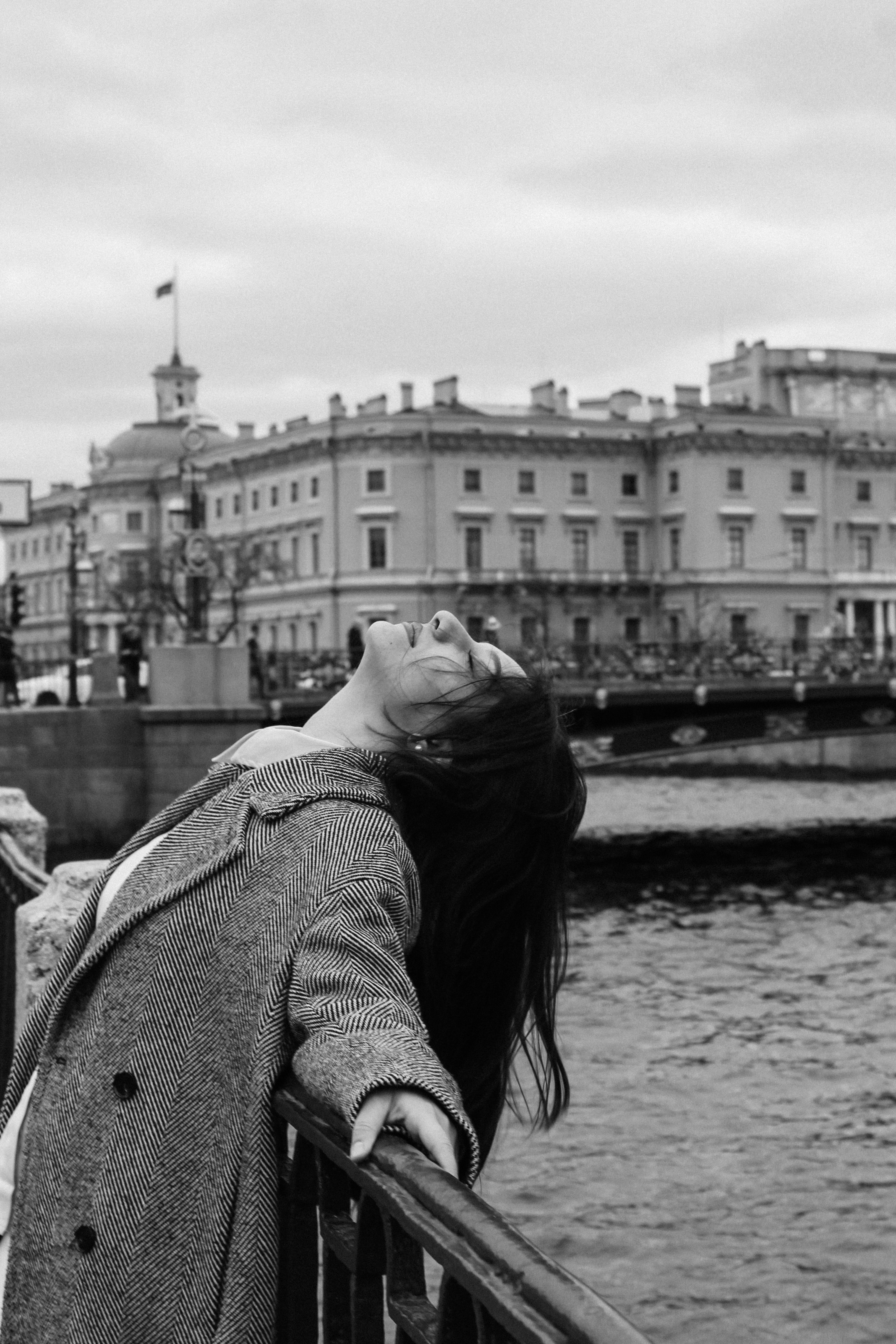 Black and white portrait of a woman leaning on a bridge railing in an urban setting.
