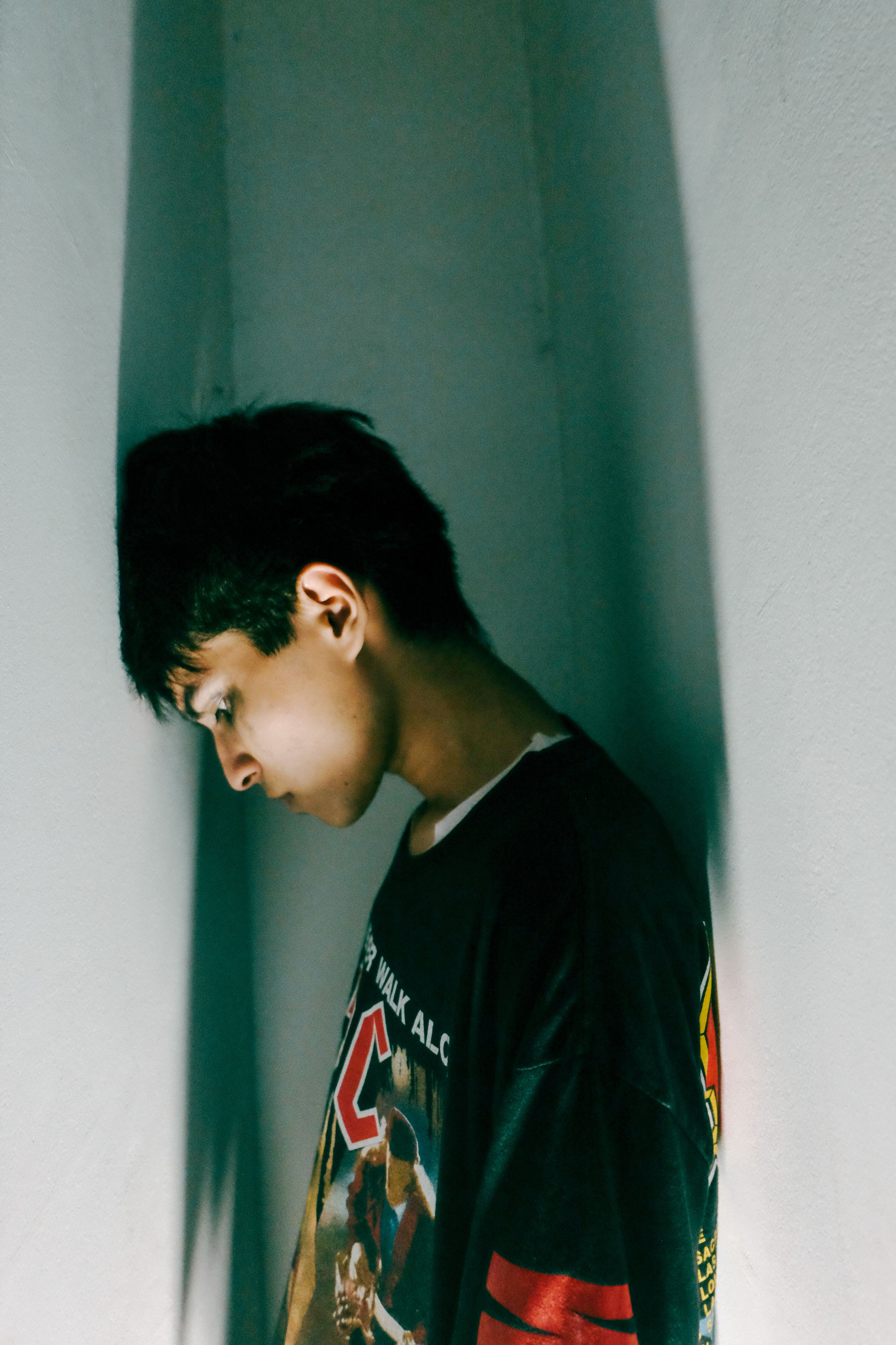 A young man leans against a white wall, deep in thought and introspection.