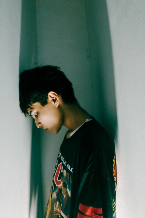 Free A young man leans against a white wall, deep in thought and introspection. Stock Photo