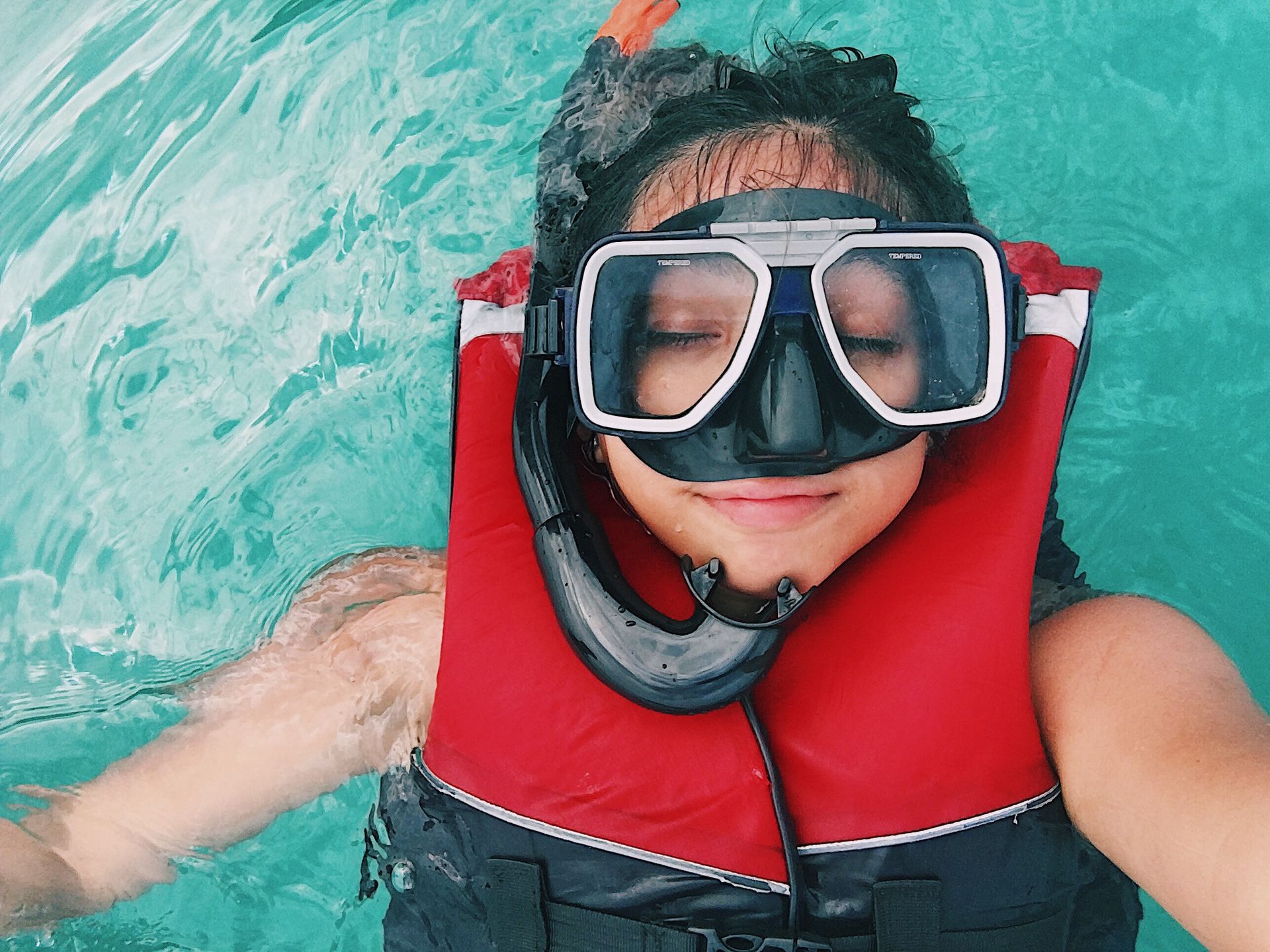 A person wearing red and black life vest and goggles while swimming