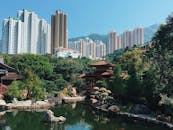 宁静的城市公园里，池塘坐落于传统建筑与蓝天下的摩天大楼之间