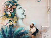 一名年轻女子在一幅色彩缤纷的壁画旁摆姿势，壁画上画着戴花卉头饰的巨嘴鸟