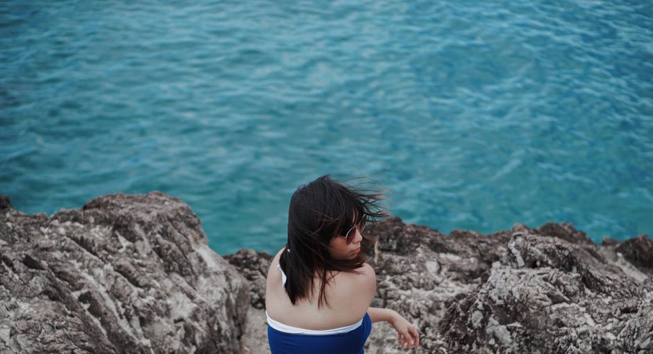 Woman in sunglasses sits on a rocky cliff enjoying the ocean view.