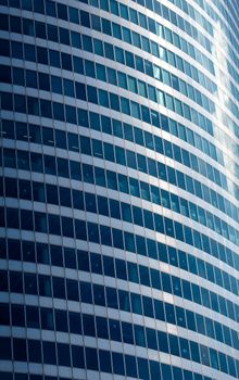 Abstract view of a modern office building with blue-tinted glass windows and a curved facade.