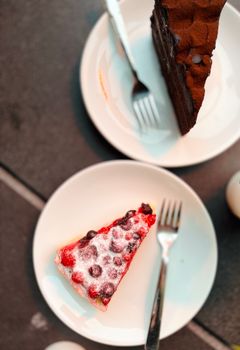 Two slices of cake on plates with forks, showcasing chocolate and berry toppings.