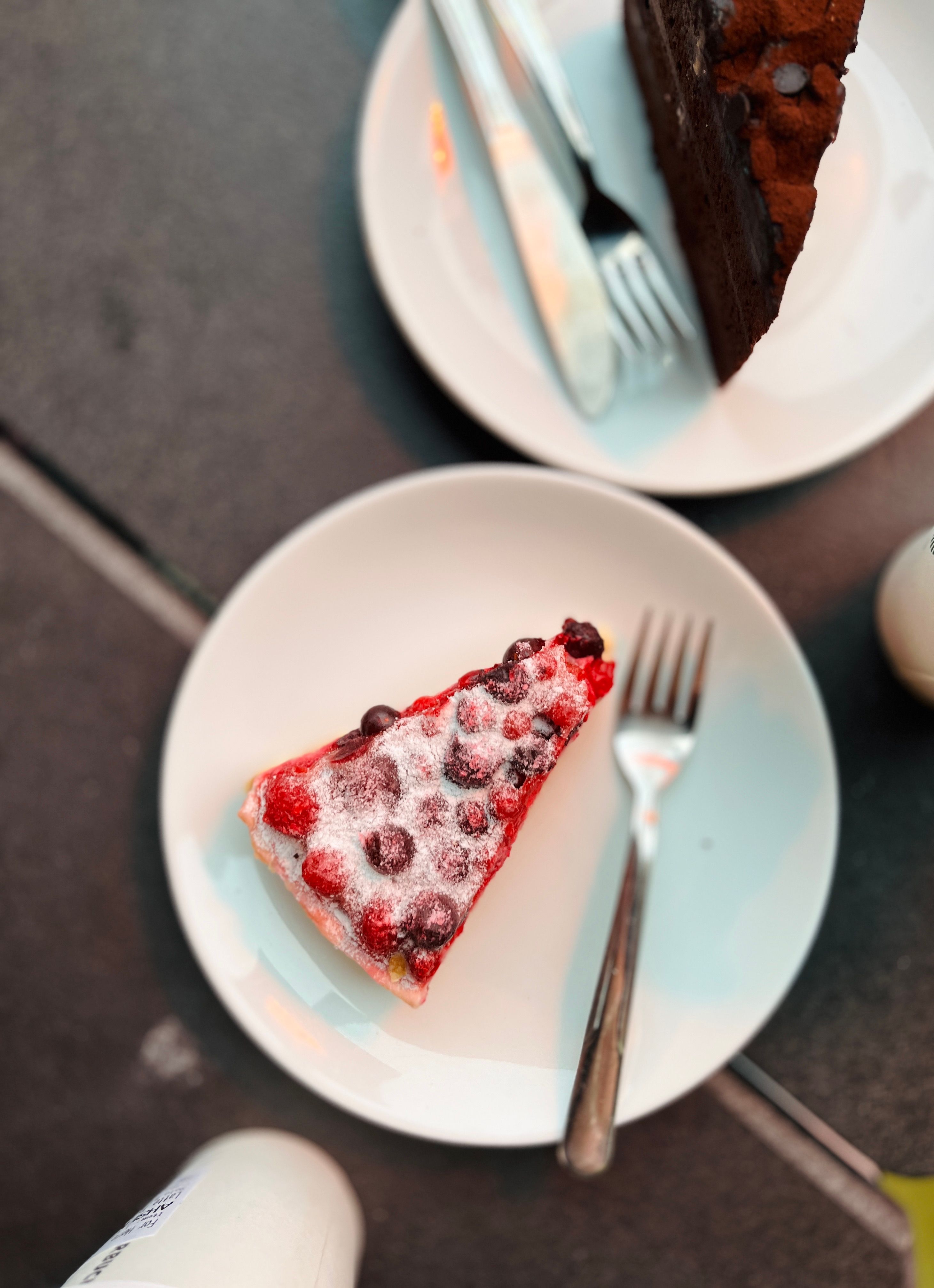 Top view of berry and chocolate cake slices on plates with forks, perfect for dessert lovers.