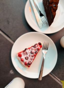 Top view of berry and chocolate cake slices on plates with forks, perfect for dessert lovers.