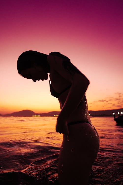 A woman in a bikini standing in the water at sunset