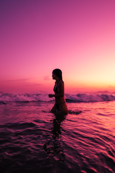 A young woman enjoys a sunset swim, surrounded by vibrant ocean waves.