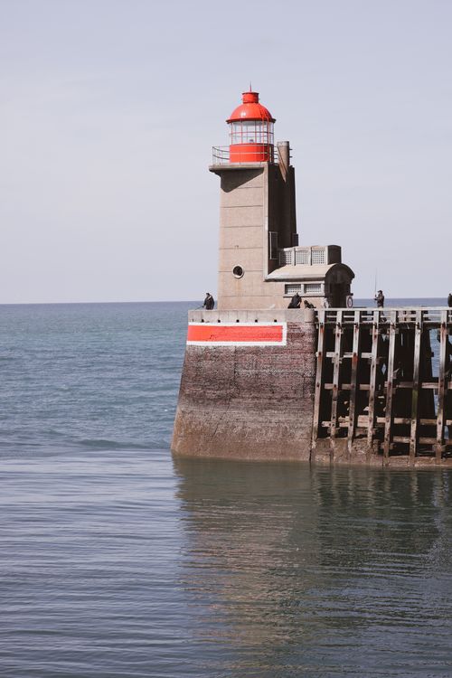 Free A picturesque lighthouse with a red top stands tall on a pier overlooking the calm sea. Stock Photo